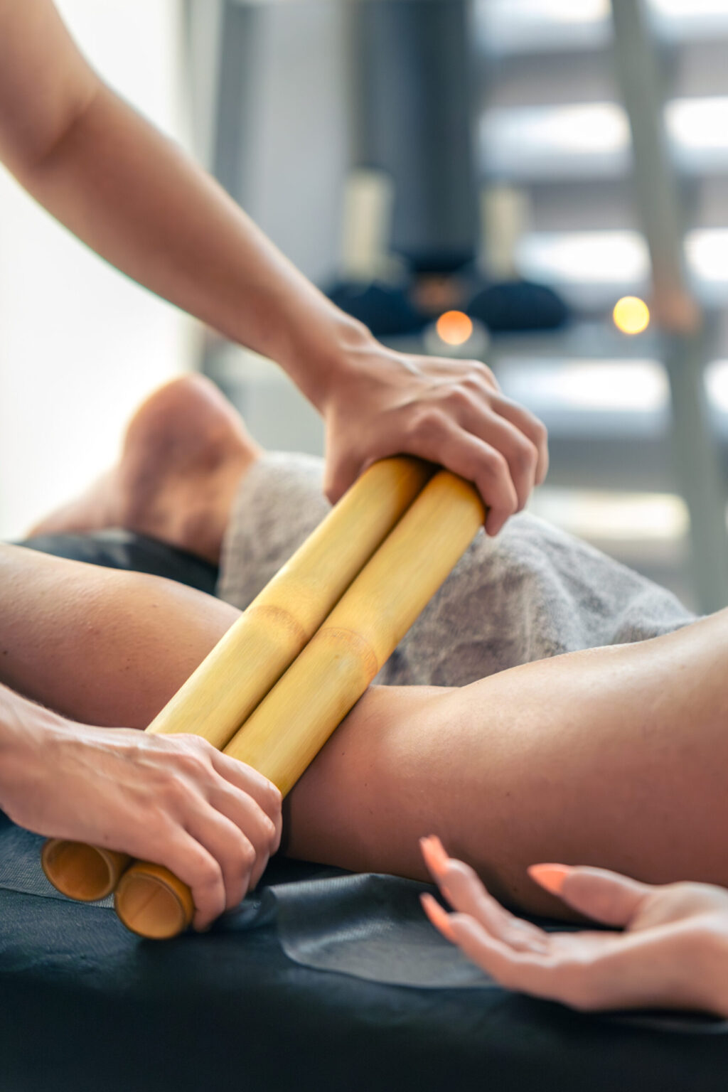 Close up of bamboo sticks working on the thigh during a session. Lymphatic drainage boosts firmness and smooth texture in a trendy wellness approach.
